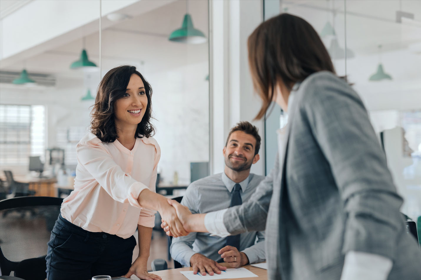 Two women shaking hands with a guy looking on