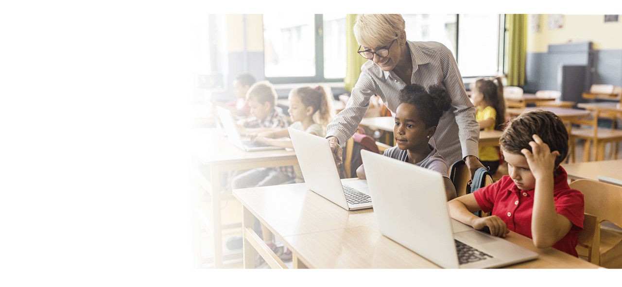 A teacher helping students during an assignment using their laptops