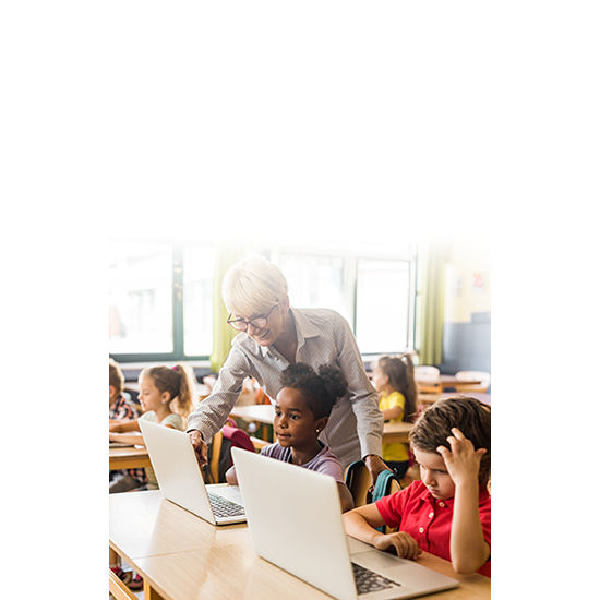 A teacher helping students during an assignment using their laptops